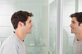 Young man smiling at self in bathroom mirror