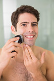 Smiling handsome shirtless man shaving with electric razor