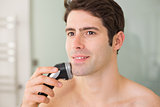 Smiling handsome shirtless man shaving with electric razor