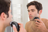 Reflection of shirtless man shaving with electric razor