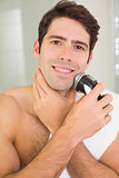 Smiling shirtless man shaving with electric razor