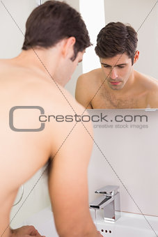 Rear view of tensed shirtless man at washbasin