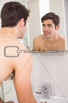 Rear view of a young smiling at self in bathroom mirror
