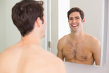 Reflection of shirtless man smiling in bathroom