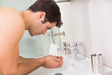 Shirtless young man washing face in bathroom