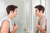 Smiling man with reflection shaving in bathroom