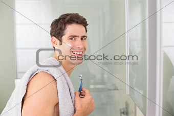Portrait of smiling handsome man shaving in bathroom