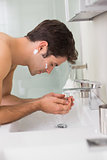 Side view of young man washing face in bathroom