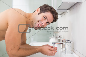 Portrait of shirtless man washing face in bathroom