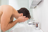 Side view of shirtless man washing face in bathroom