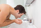 Side view of shirtless man washing face in bathroom