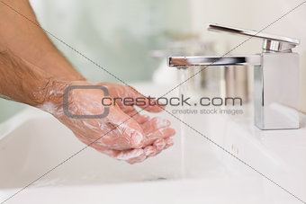 Washing hands with soap under running water at bathroom sink