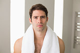 Shirtless young man with towel around neck at home