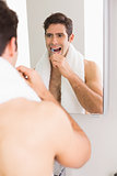 Young shirtless man with reflection brushing teeth