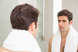 Tensed young man looking at self in bathroom mirror