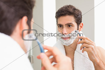 Young man with reflection shaving in the bathroom
