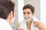 Young man with reflection shaving in bathroom