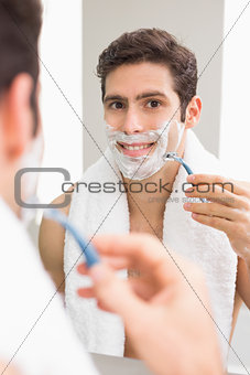 Young man with reflection shaving in bathroom