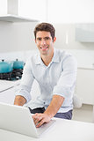 Smiling casual young man using laptop in kitchen