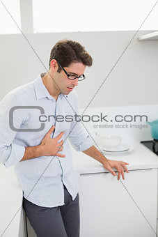 Casual man with stomach pain standing in the kitchen