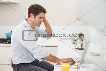 Concentrated casual man using laptop in kitchen