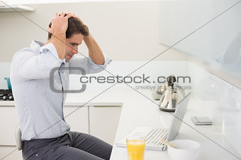 Concentrated casual young man using laptop in kitchen