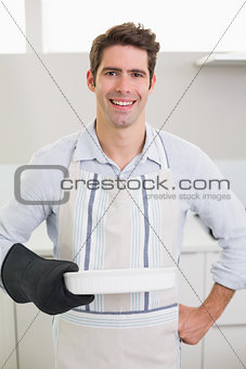 Smiling handsome man holding a baking dish in kitchen