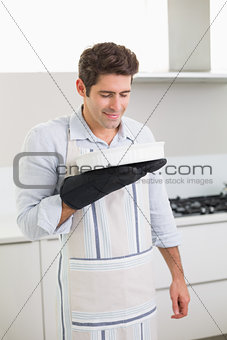 Man smelling food in baking dish in kitchen