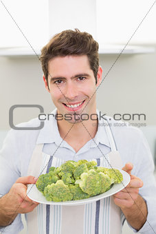 Smiling man holding a plate of broccoli in kitchen