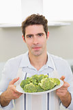 Handsome man holding a plate of broccoli in kitchen