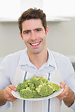 Smiling man holding a plate of broccoli in kitchen