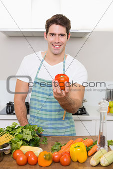 Smiling man holding bell pepper with vegetables in kitchen