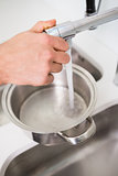 Hand filling pan with water at kitchen sink