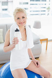 Woman with water bottle sitting on exercise ball