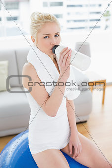 Fit woman drinking water while sitting on exercise ball