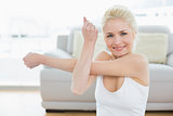 Smiling sporty woman stretching hand in fitness studio