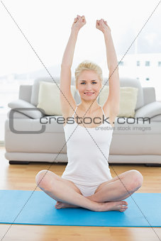 Smiling sporty woman stretching hands upward in fitness studio
