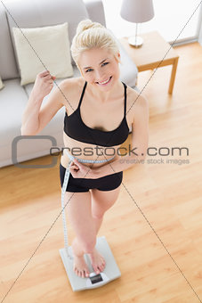 Woman in sportswear standing on scale while measuring waist