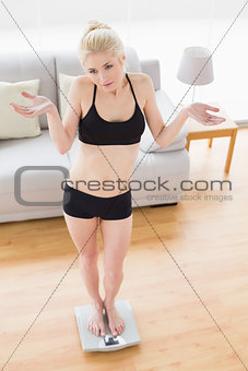 Unsure young woman in sportswear standing on scale