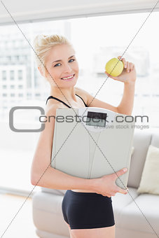 Smiling fit woman in sportswear holding scale and apple