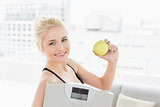 Fit woman holding scale and apple in fitness studio