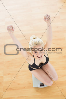 Cheerful fit woman on scale in fitness studio