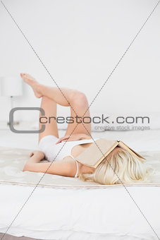 Young woman with book over face resting in bed