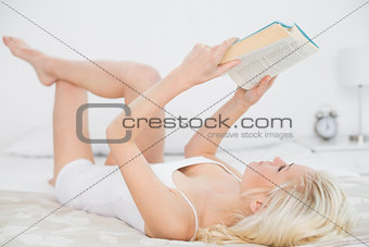 Relaxed young woman reading a book in bed