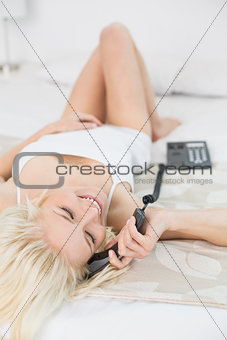 Relaxed smiling woman using telephone in bed