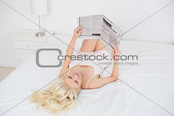 Overhead view of blond reading newspaper in bed