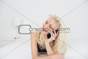 Cheerful blond using mobile phone in bed
