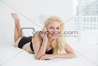 Young woman in lingerie using mobile phone in bed