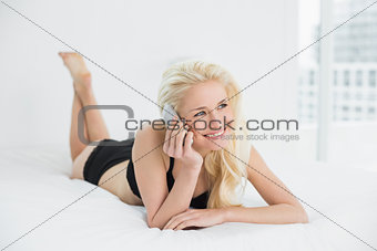 Smiling woman in lingerie using mobile phone in bed