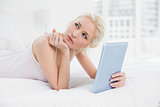 Thoughtful casual blond with tablet PC lying in bed